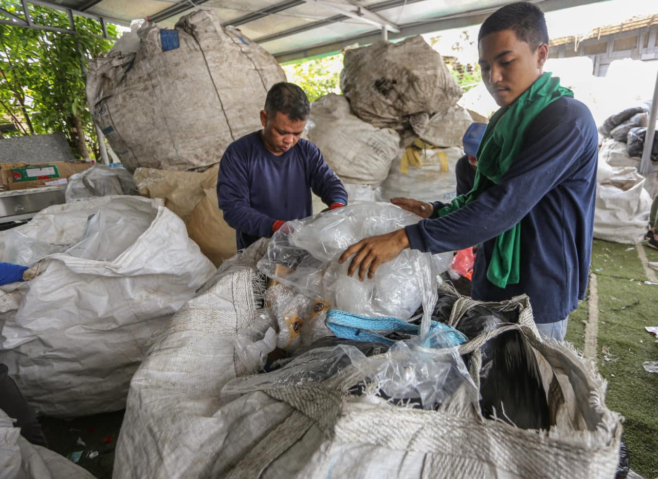 Philippine men working on filling up plastic in large bags - The plastic flamingo plastic recyclers