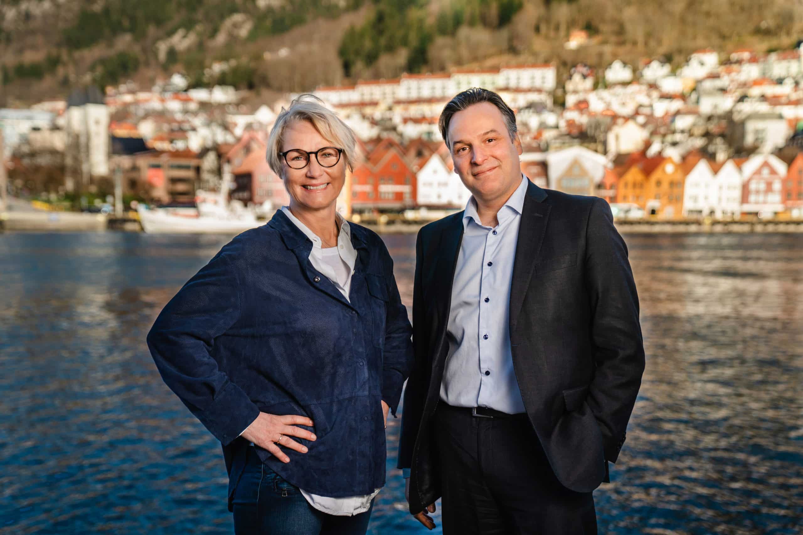 Two people stands smiling with Bergen in the background - Elisabeth Grieg and Matthew Duke