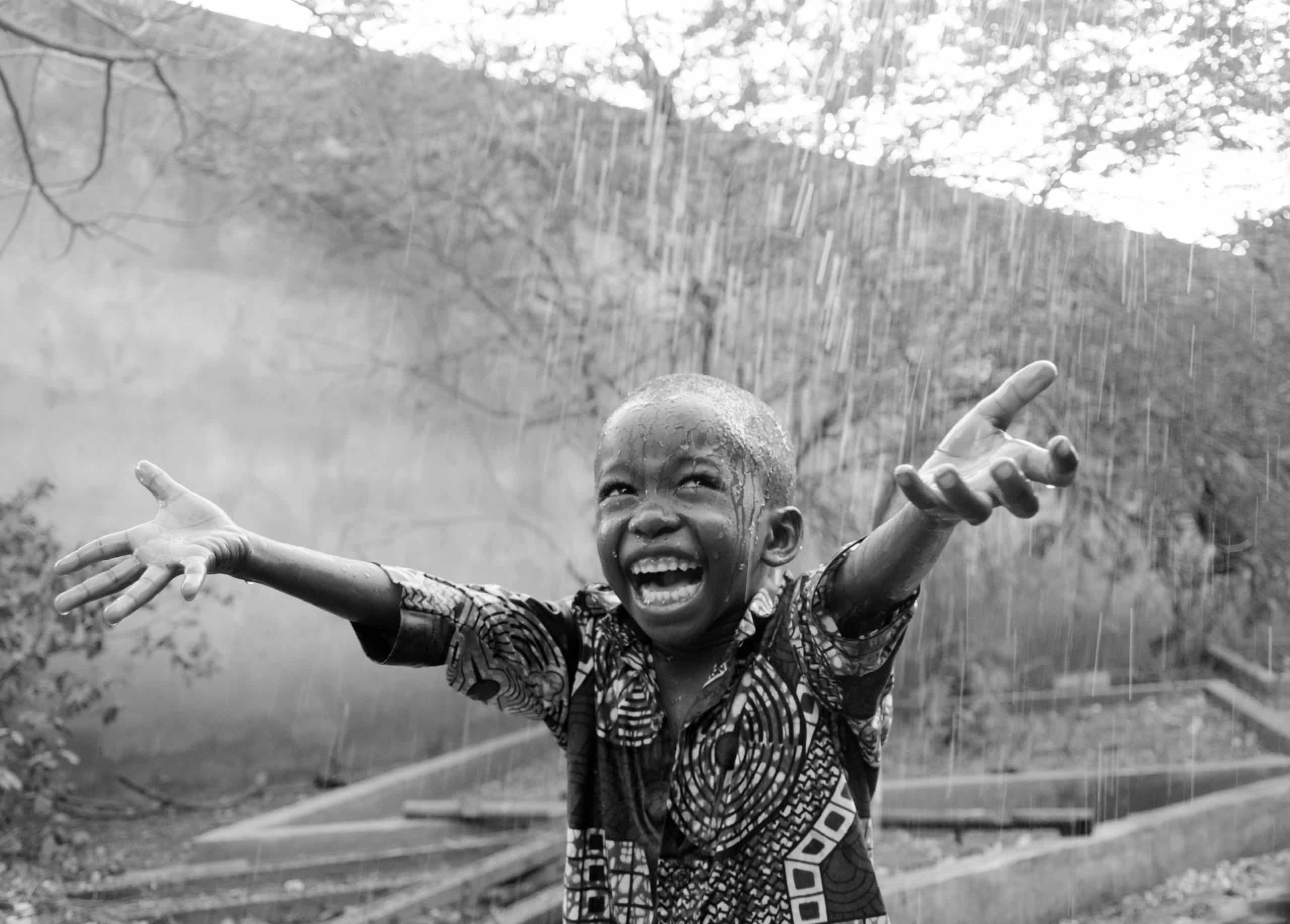African child stretching out his arms in the rain.