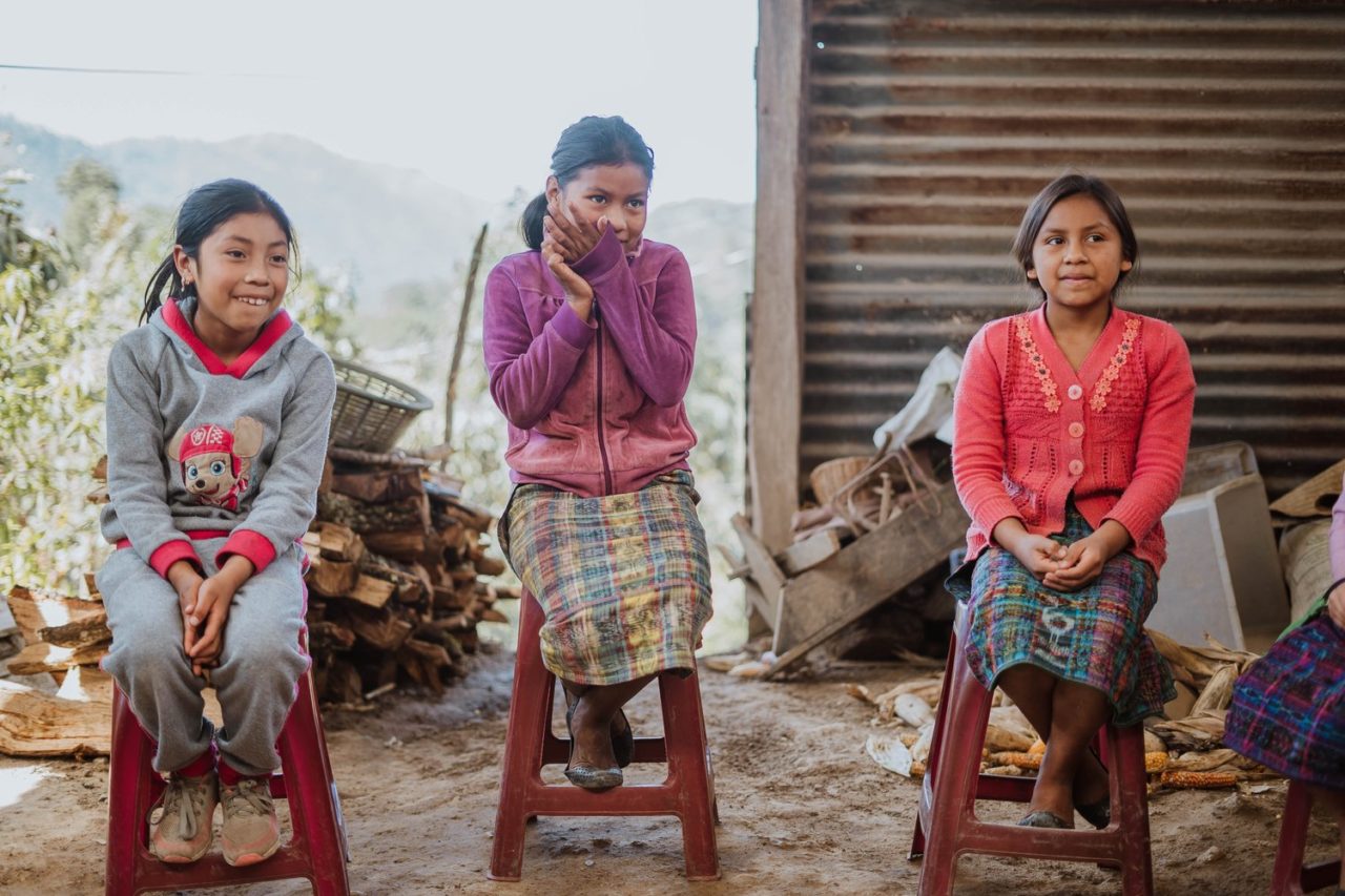 Three young girls sitting on plastic chairs outside in Guatemale - Grieg Foundation