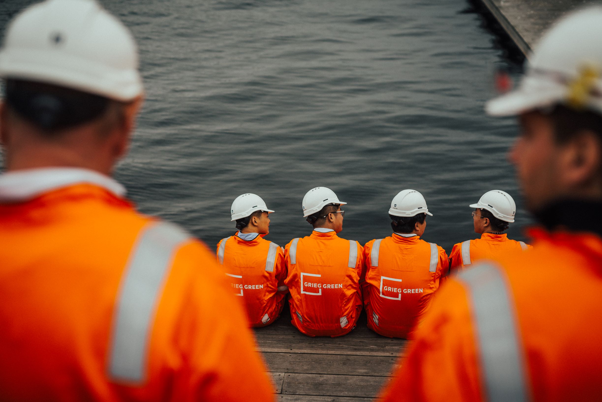 Grieg Green employees in orange uniforms sitting by the ocean.