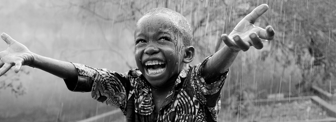 African child stretching out his arms in the rain